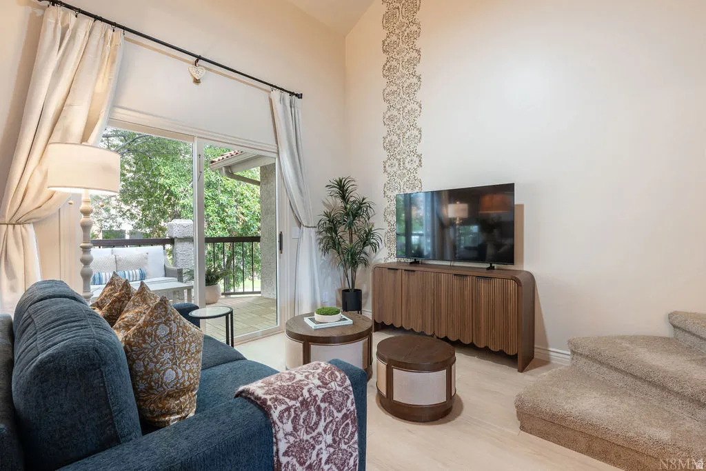 Living area featuring light-tone flooring, a patterned accent wall, and a wood-finish media console