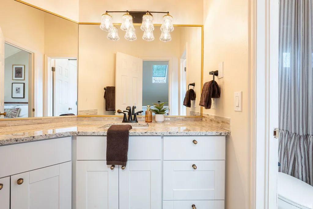 Vanity with white shaker cabinetry, gold-tone hardware, and a speckled countertop