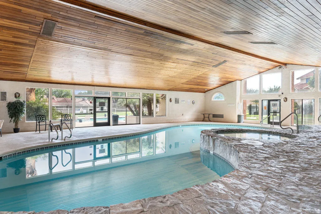 Indoor swimming pool featuring a curved design, adjacent hot tub with stone-finish surround, and expansive windows