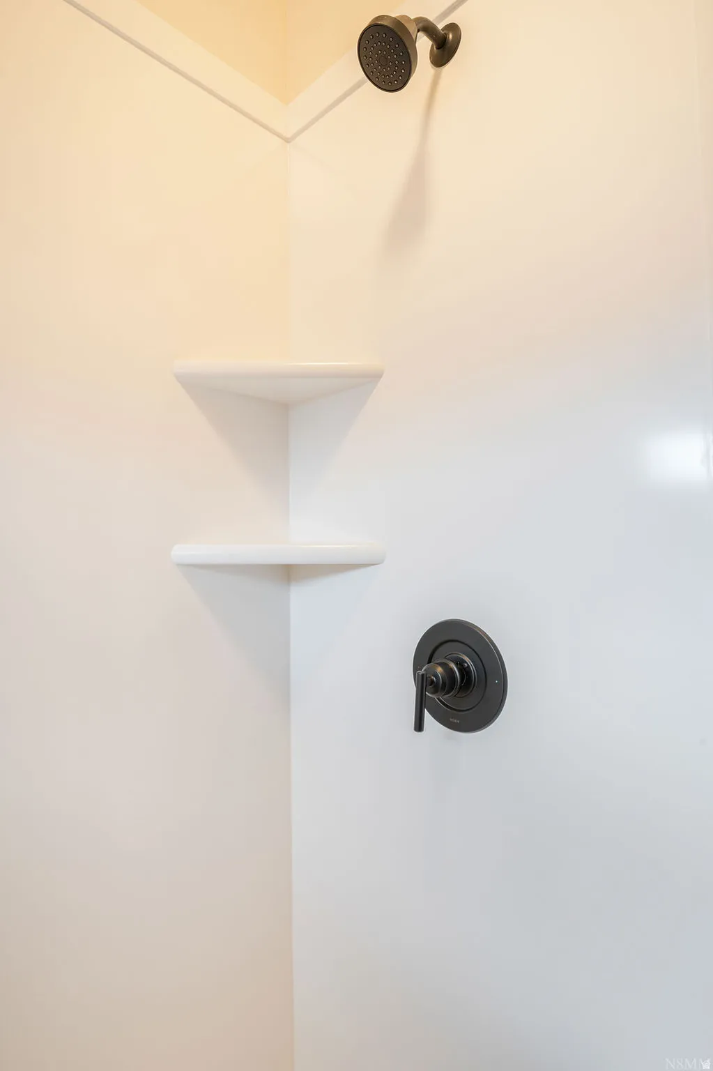 Shower enclosure featuring white paneling, integrated corner shelving, and matte black fixtures