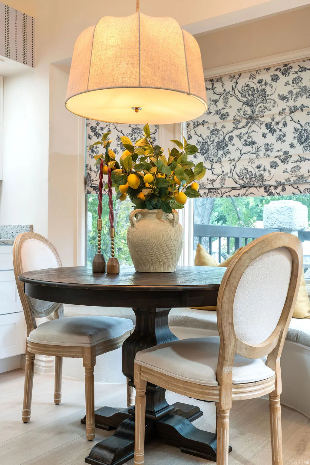 Wood-finish flooring, built-in window seating, patterned Roman shade, and drum pendant lighting