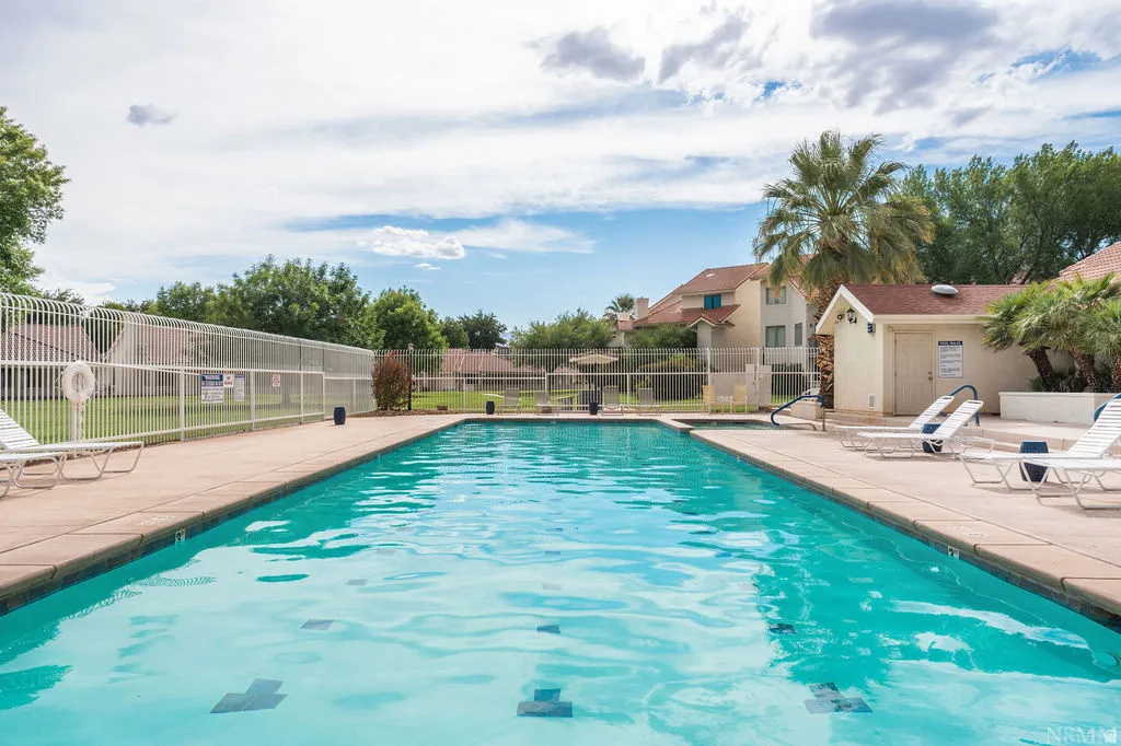 Outdoor swimming pool with a concrete surround, white perimeter fencing, and a dedicated pool house