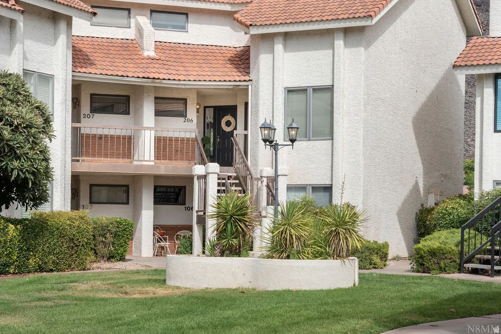 Multi-story stucco exterior with red tile roofing, featuring an exterior staircase, balcony with wood-finish railing, and a ground-level patio area