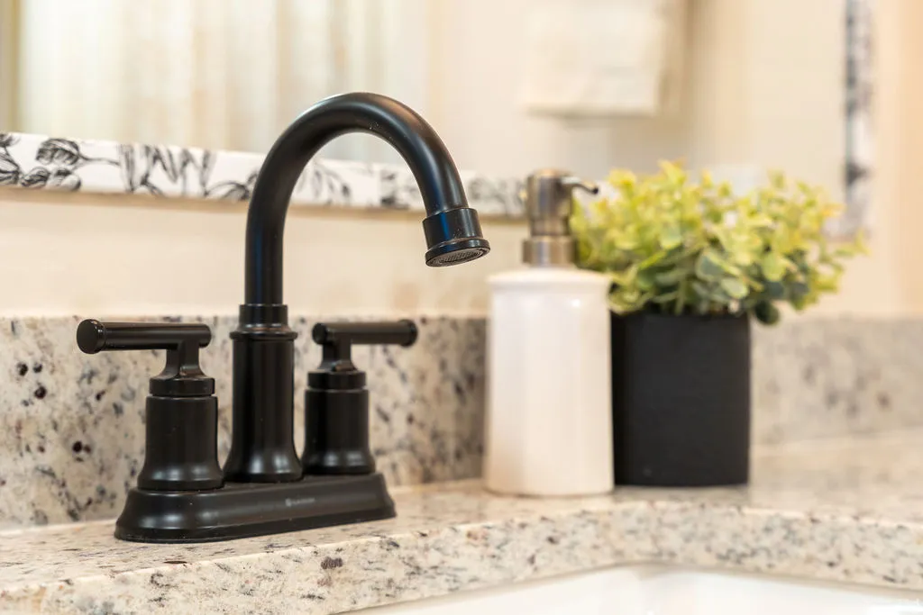 Black-finish faucet with dual handles, set in a speckled countertop, and a white porcelain sink