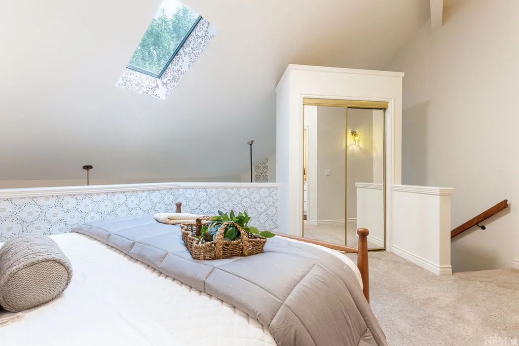 Angled skylight, vaulted ceiling, patterned accent wall, sliding mirrored closet doors, and carpeted flooring