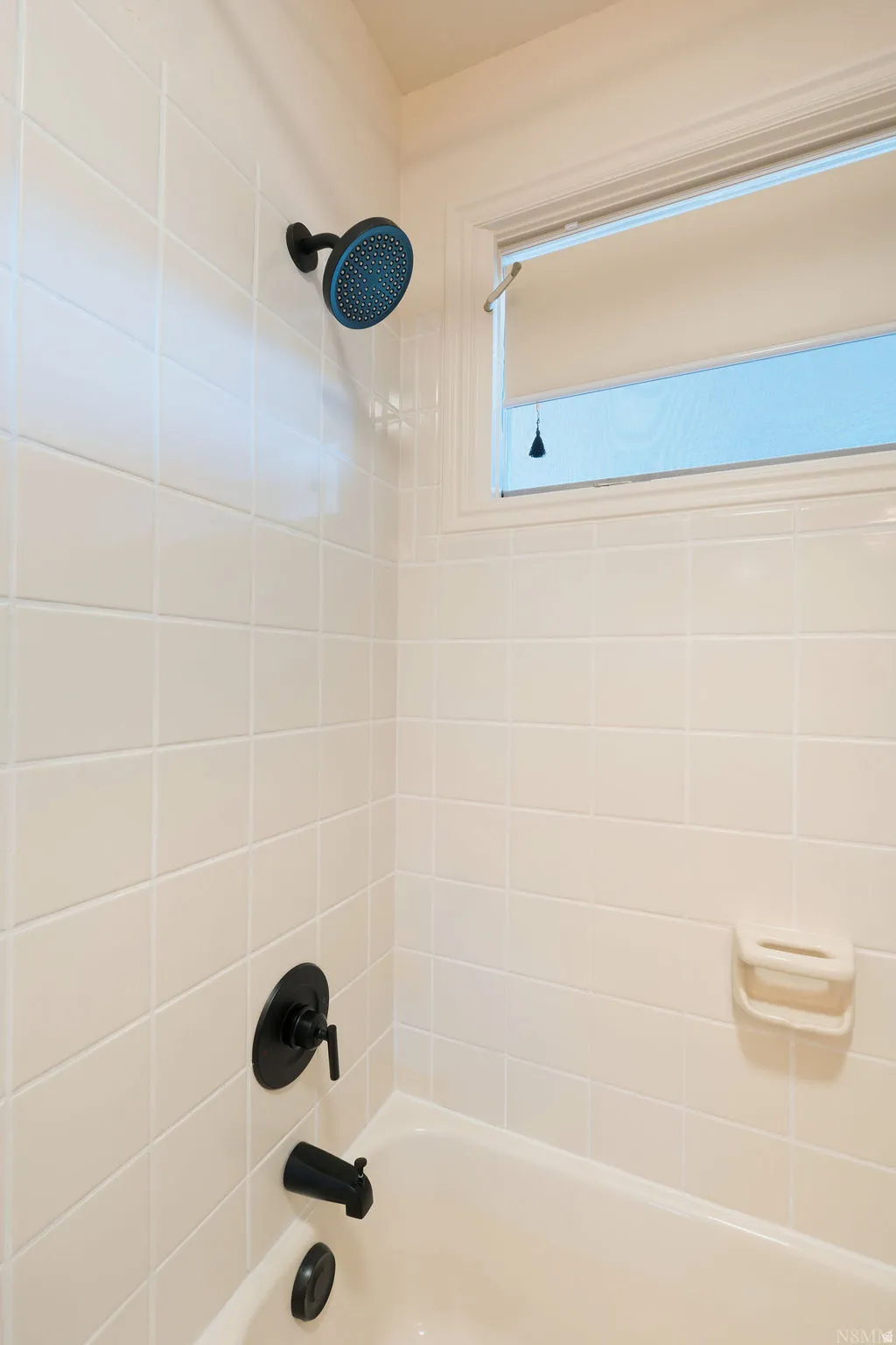 Bathtub with white tile surround, black-finish shower head, and black-finish tub fixtures