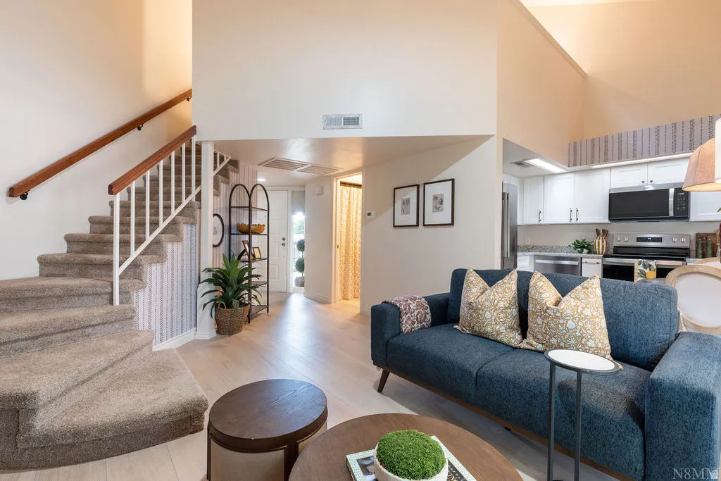 Vaulted ceilings, wood-finish flooring, white kitchen cabinetry, stainless steel appliances, and a carpeted staircase with wood handrails
