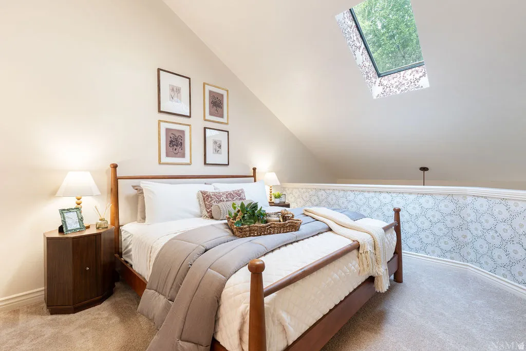 Vaulted ceiling with skylight, patterned half-wall, wood-finish flooring, and built-in wall sconce