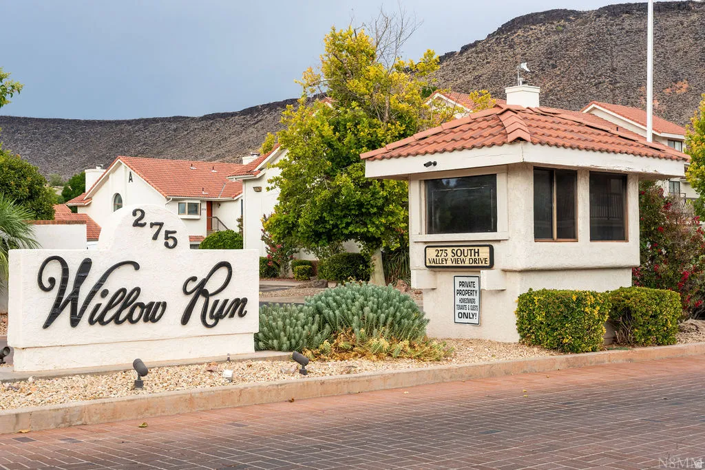 Entryway featuring a stucco sign, mature landscaping, and a guardhouse with a tiled roof