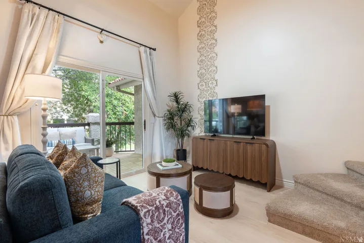 Living area featuring light-tone flooring, a patterned accent wall, and a wood-finish media console