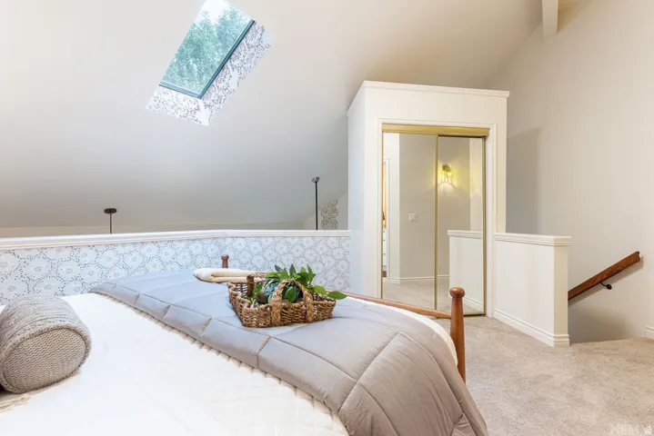Angled skylight, vaulted ceiling, patterned accent wall, sliding mirrored closet doors, and carpeted flooring