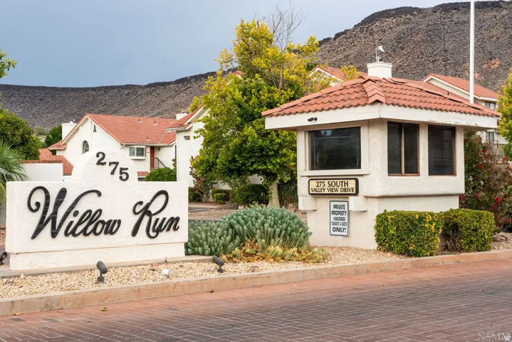 Entryway featuring a stucco sign, mature landscaping, and a guardhouse with a tiled roof