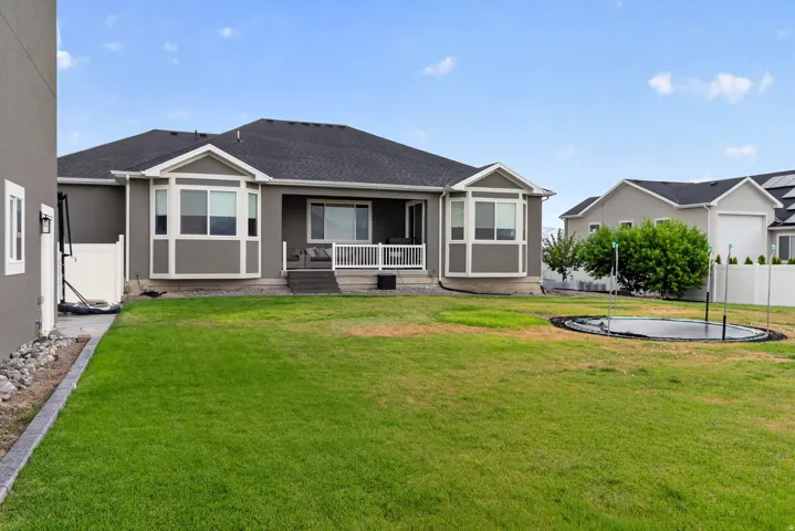 Expansive backyard featuring a manicured lawn, a raised deck with white railing, and multiple bay windows