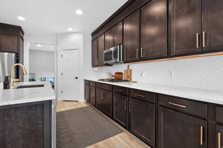 Kitchen featuring dark wood-finish cabinetry, white countertops, stainless steel appliances, and a tile backsplash