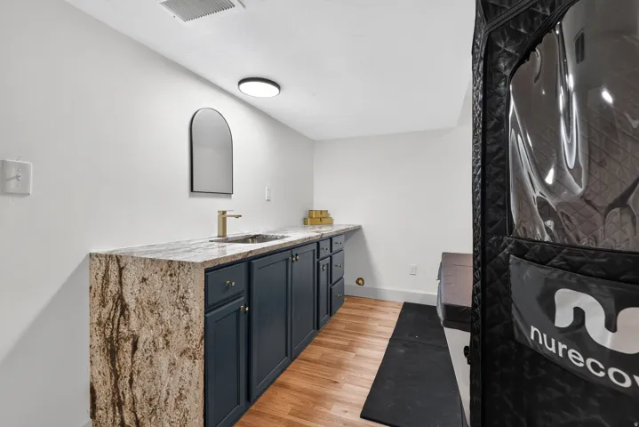 Built-in vanity with stone countertop, undermount sink, brass-finish faucet, and blue cabinetry