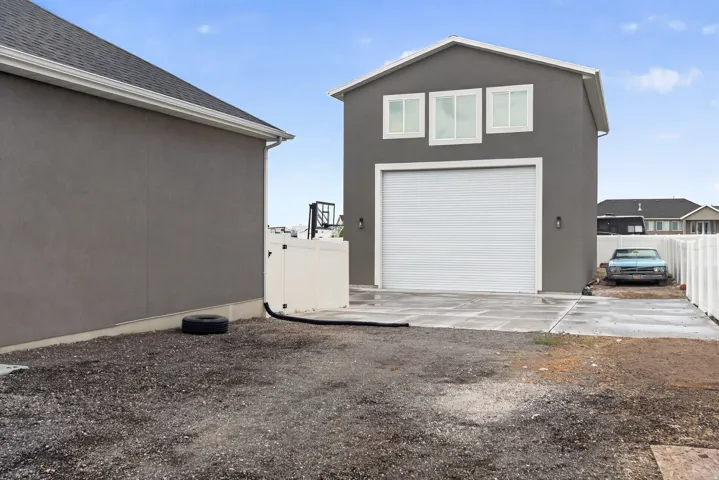 Detached structure with stucco exterior, three upper-level windows, and a roll-up garage door with integrated lighting