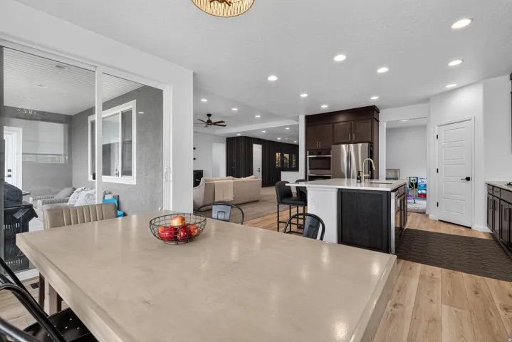 Open-concept living area featuring wood-finish flooring, recessed lighting, and a kitchen with dark cabinetry, stainless steel appliances, and a central island with counter seating
