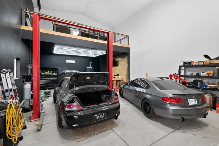 Two-story garage space with a vehicle lift system, polished concrete flooring, a mezzanine level with metal cable railings, and track lighting