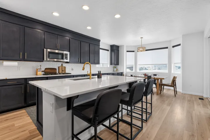 Modern kitchen featuring dark cabinetry, stainless steel appliances, a center island with countertop seating, wood-finish flooring, and a dining area with a bay window