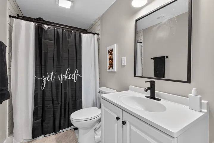 White vanity with integrated sink, matte black faucet, framed mirror, and tiled shower surround