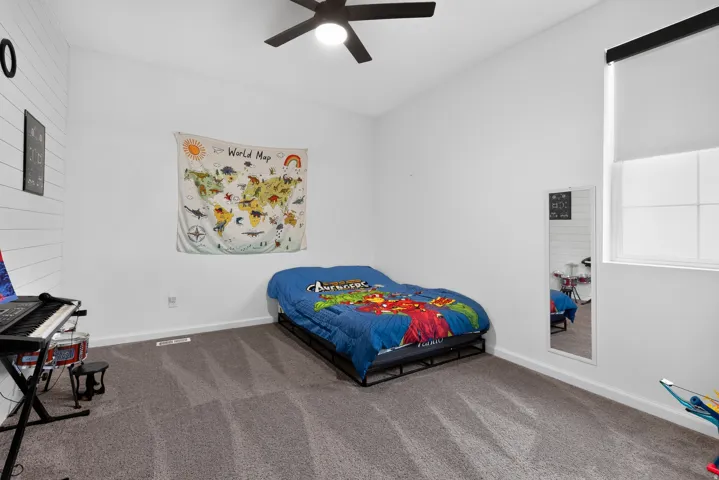 Carpeted flooring, white walls, window with roller shade, ceiling fan with light fixture, and an accent shiplap wall