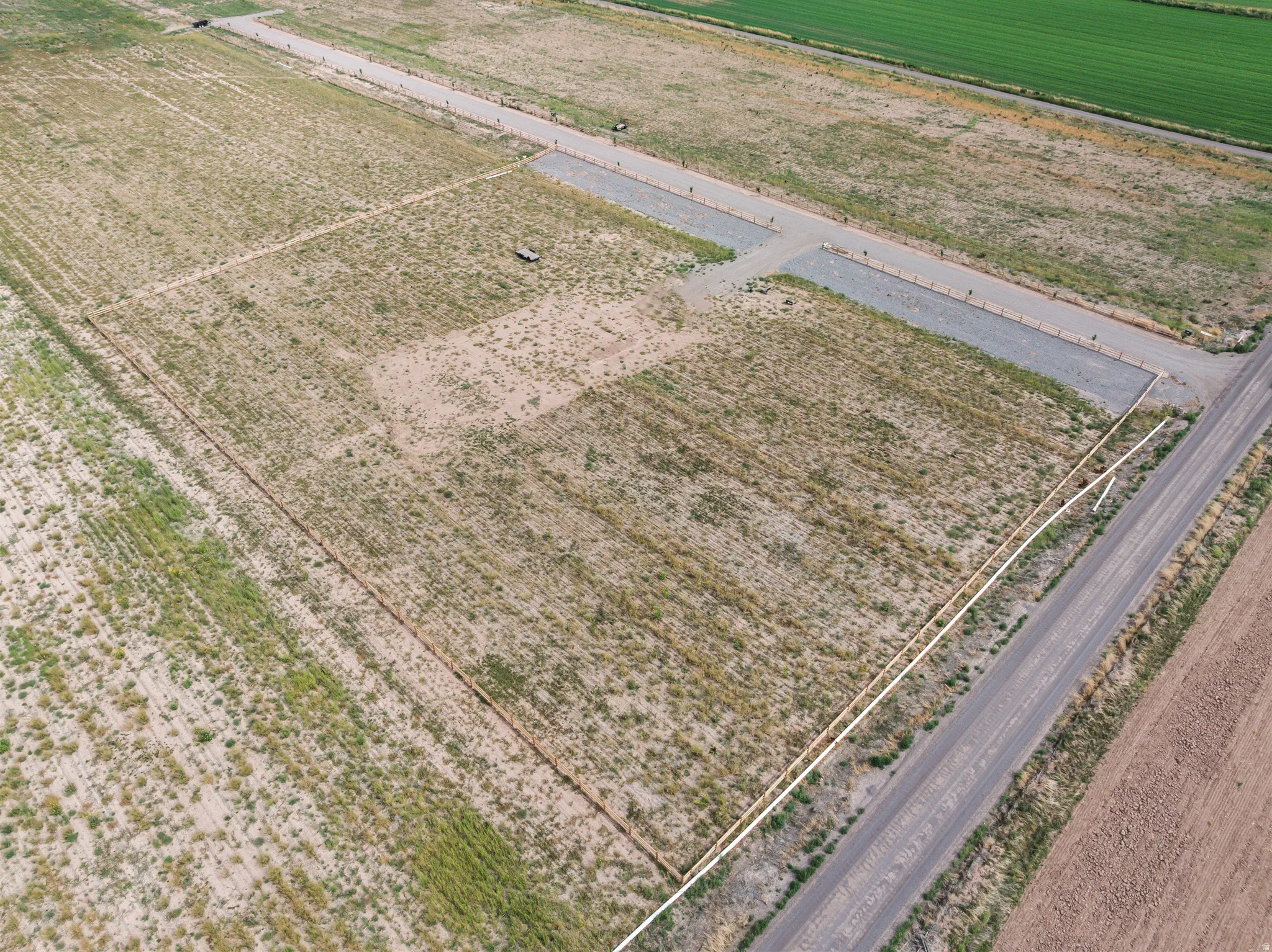 Expansive land parcel featuring a gravel road, delineated property lines, and an adjacent paved road