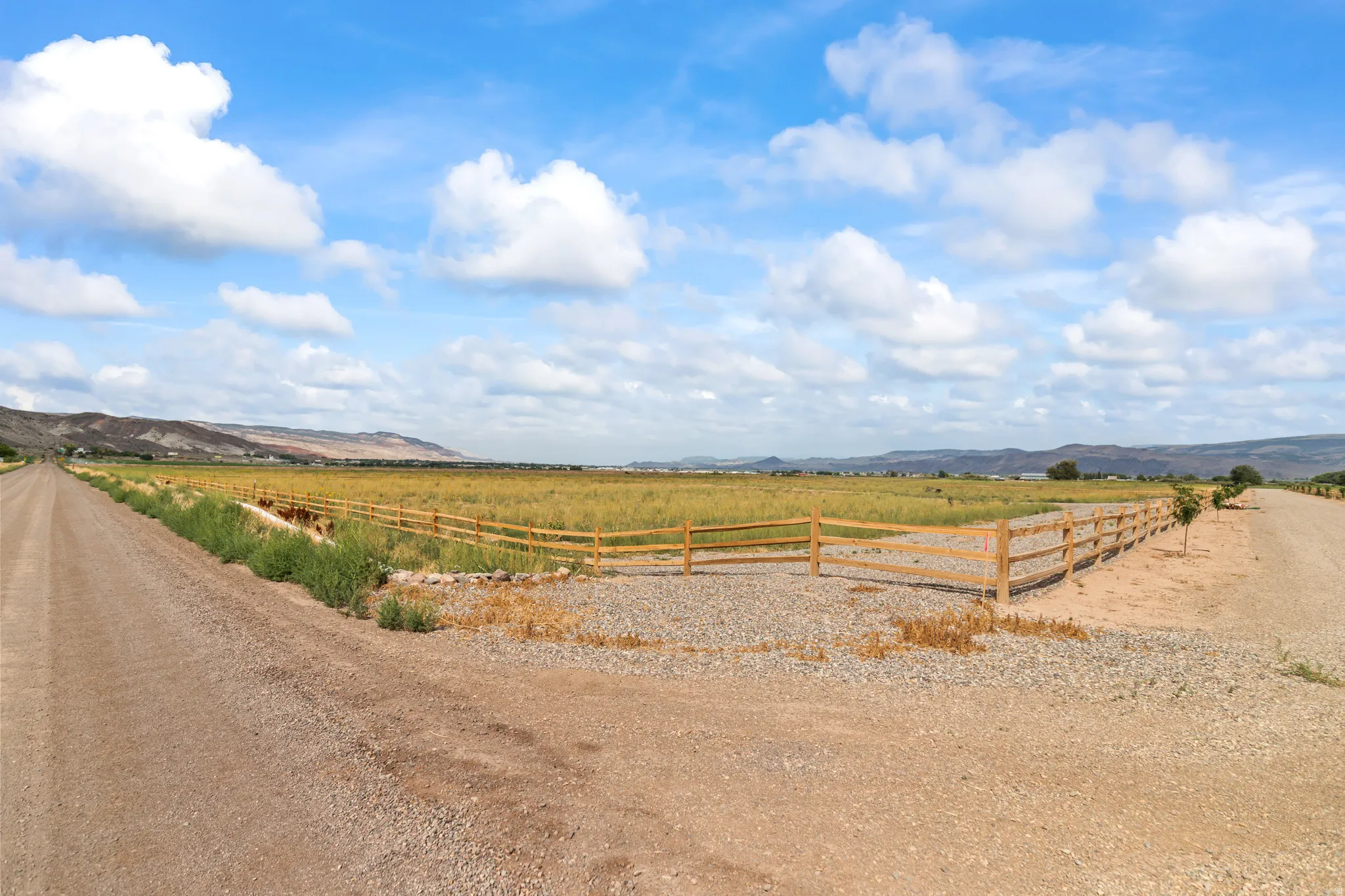 Expansive property featuring a natural wood split-rail fence, gravel driveways, and distant mountain ranges