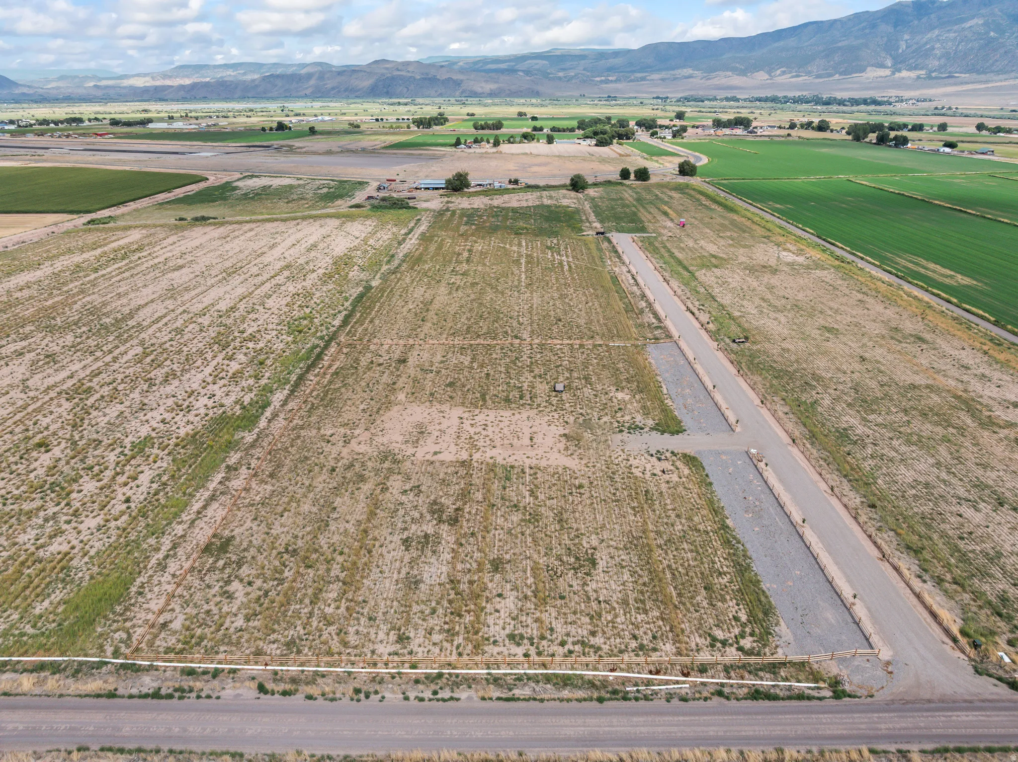Expansive agricultural land featuring a gravel road, surrounding green fields, and distant mountains