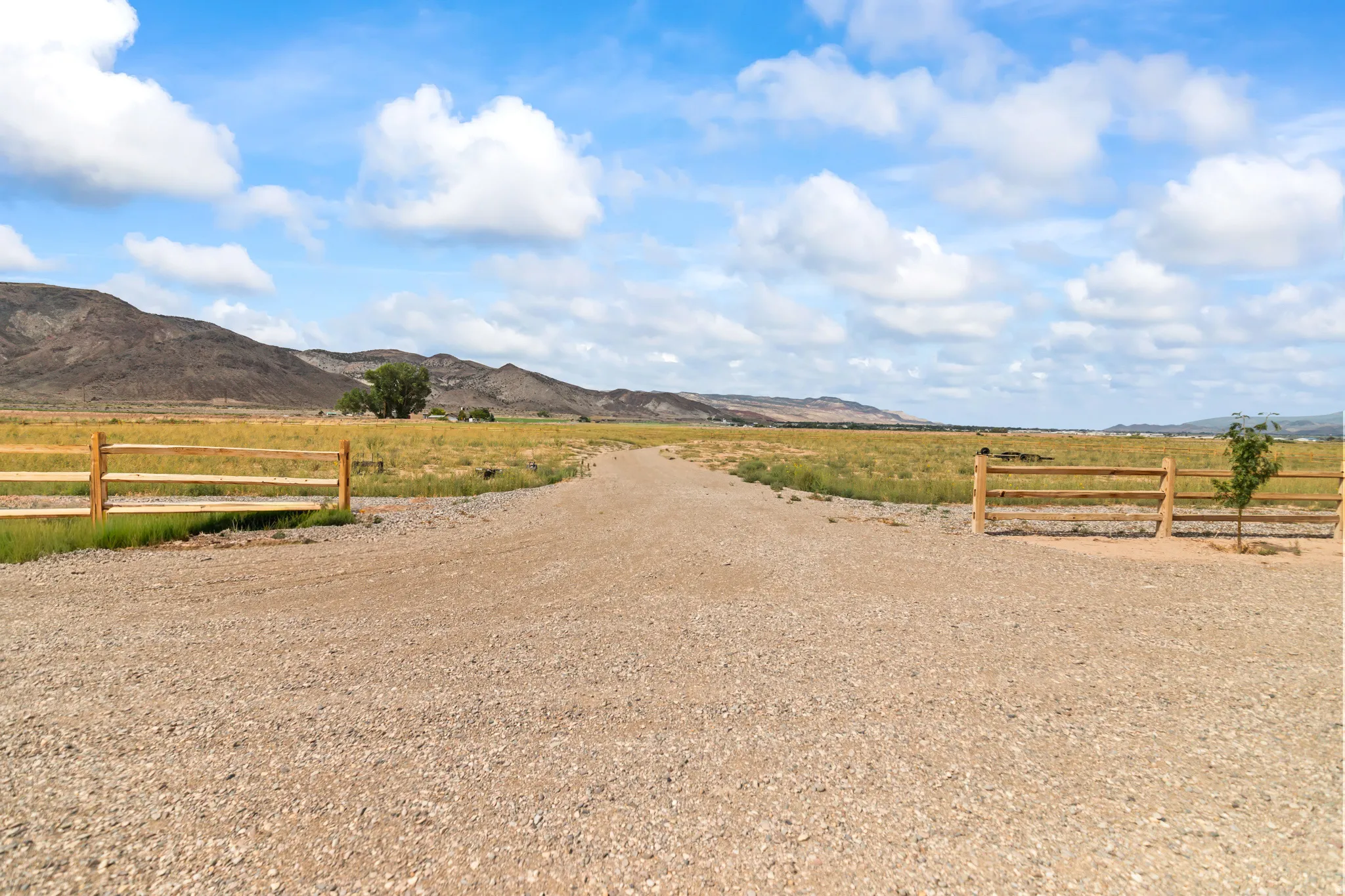 Gravel driveway with natural wood fencing and expansive open fields