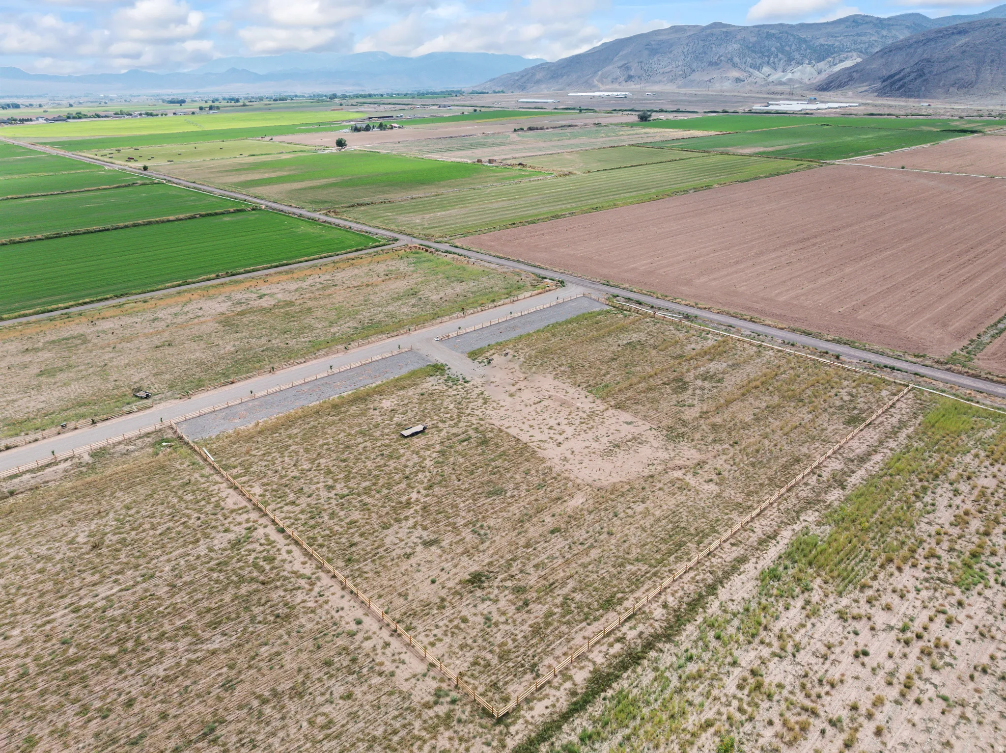Expansive land parcel featuring partial fencing, gravel access roads, and distant mountain scenery