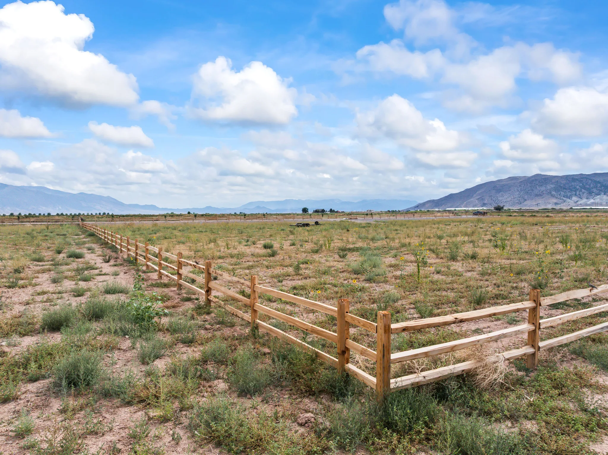 Expansive acreage featuring a natural wood split-rail fence, open terrain, and distant mountain backdrops