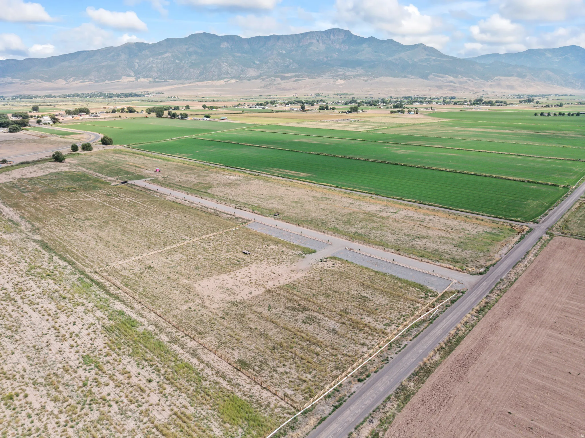 Expansive undeveloped land with mountain backdrop, surrounded by green agricultural fields and an unpaved road