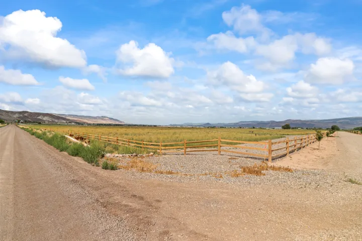 Expansive property featuring a natural wood split-rail fence, gravel driveways, and distant mountain ranges