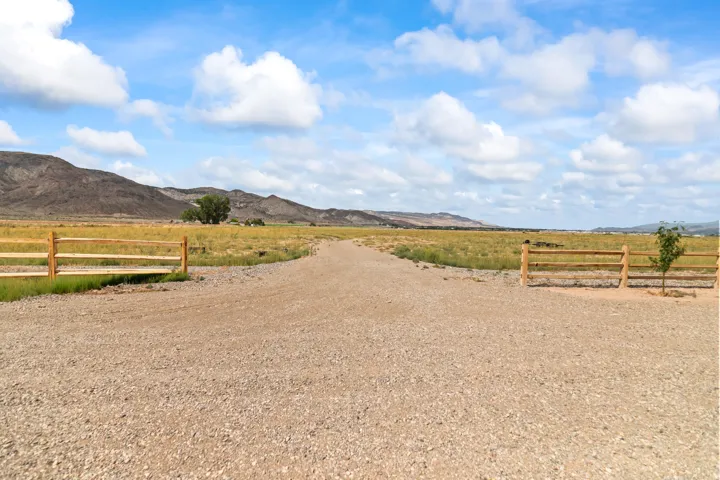 Gravel driveway with natural wood fencing and expansive open fields