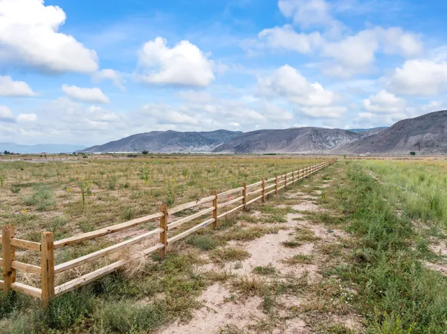 Expansive land featuring a natural wood split rail fence, uncultivated terrain, and distant mountain ranges under a partly cloudy sky