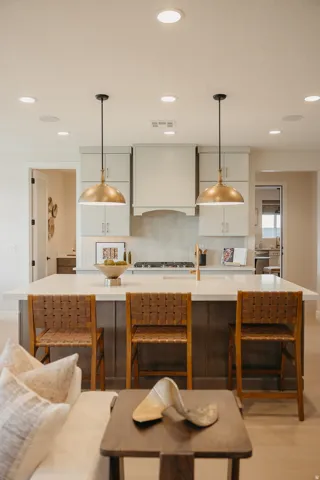 Kitchen island with seating, pendant lighting, recessed lighting, light-toned cabinetry, and a gas range