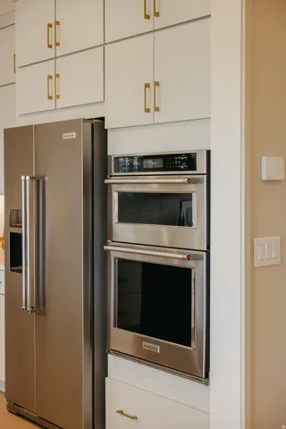 Integrated stainless steel refrigerator, built-in double oven, and white cabinetry with gold-tone hardware