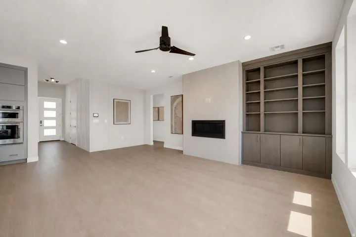 Wood-finish flooring throughout, integrated built-in shelving, linear fireplace with tiled surround, ceiling fan, and recessed lighting