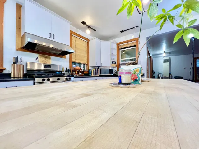 Spacious wood-finish countertop, stainless steel range with overhead ventilation, white cabinetry, and recessed lighting