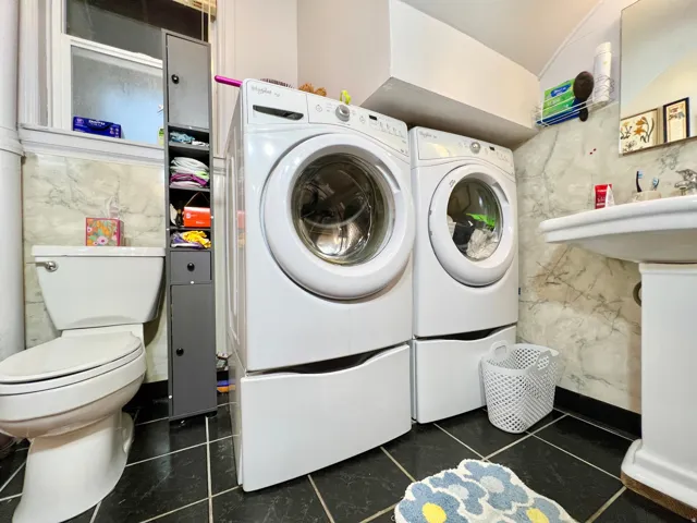 Ceramic pedestal sink, white toilet, tile flooring, and a window providing natural illumination