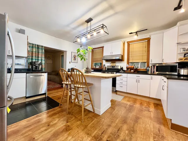 Kitchen featuring wood-finish flooring, white cabinetry, a central island with a wood countertop, and stainless steel appliances