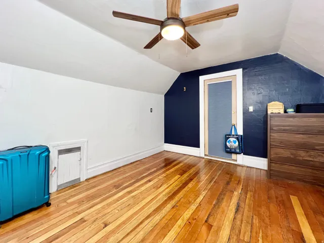 Vaulted ceiling with a wood-finish ceiling fan, wood-finish flooring, and white baseboards