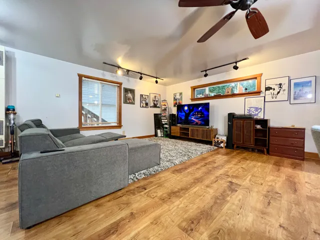 Wood-finish flooring, multiple windows providing natural light, track lighting, and a ceiling fan