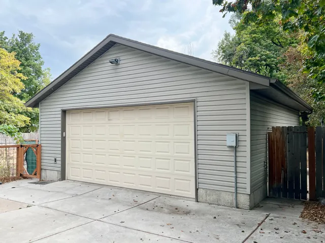 Detached garage featuring horizontal siding, a paneled garage door, a concrete driveway, and a wood privacy fence