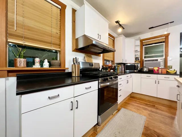 Kitchen featuring white cabinetry, black countertops, wood-finish flooring, stainless steel range, and stainless steel range hood
