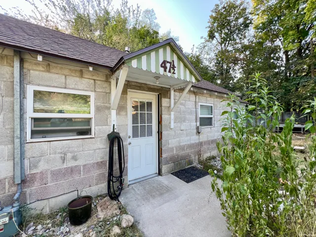 Concrete block exterior with white frame windows, a white entry door, and a striped awning