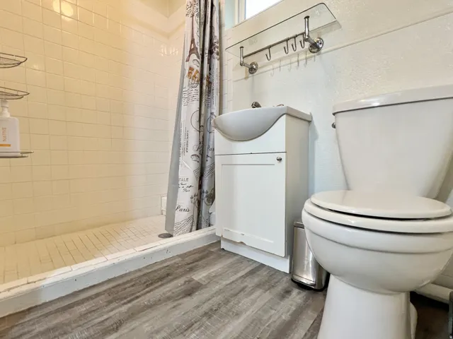 White tiled shower surround with a tiled shower pan, wood-finish flooring, white vanity with integrated sink, and white toilet