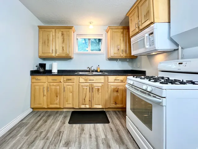Kitchen featuring wood-finish cabinetry, dark countertops, an undermount sink, and wood-look flooring
