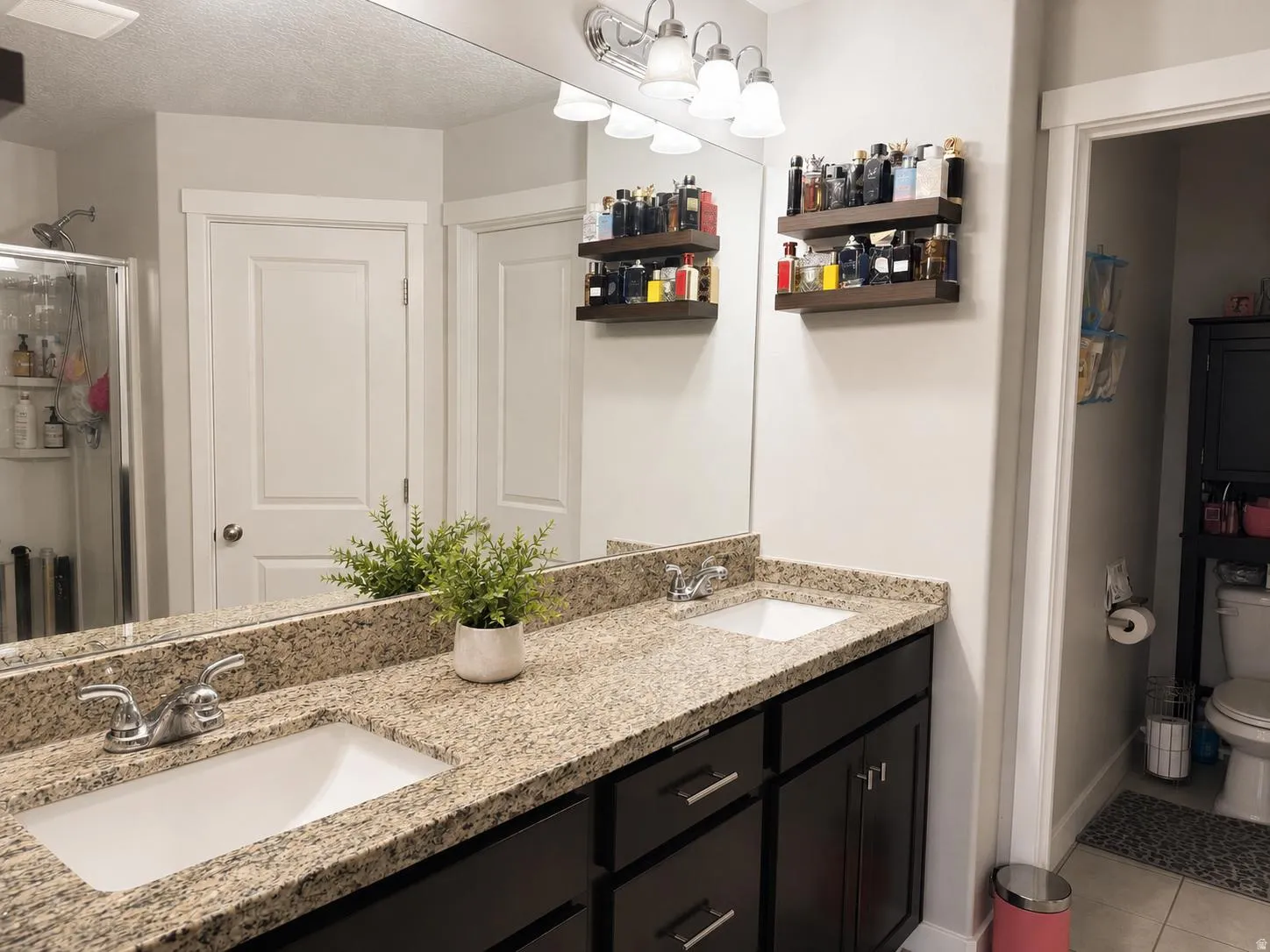 Dual vanity with granite-style countertop and undermount sinks, set below a full-width mirror with a four-light fixture