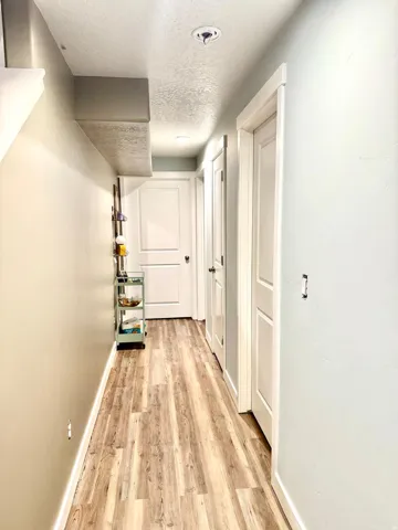 Bright hallway with clean white walls, recessed ceiling lighting, and wood-finish flooring throughout